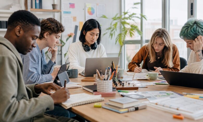 Kleine Gruppe junger Erwachsener arbeitet in unterschiedlichen Stilen gemeinsam an einem Tisch.